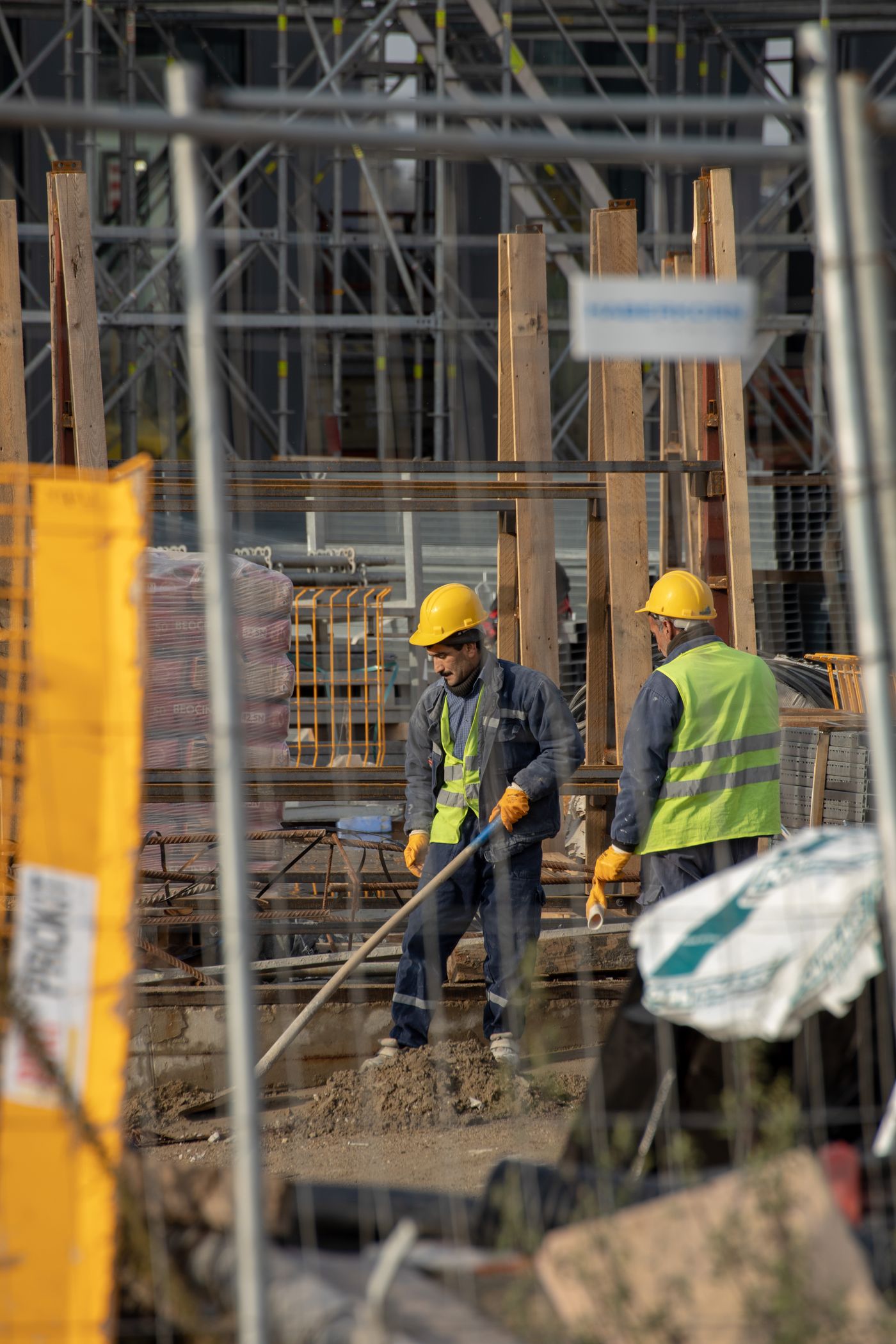 Two construction workers in hard hats and high-visibility vests preparing a building site